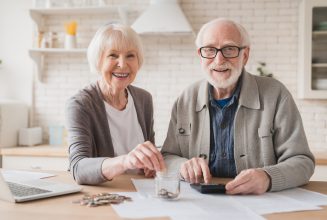 Savings concept. Nest egg of old elderly senior couple grandparents husband and wife saving money, economizing pension, mortgage loan at home using laptop and putting coin into moneybox